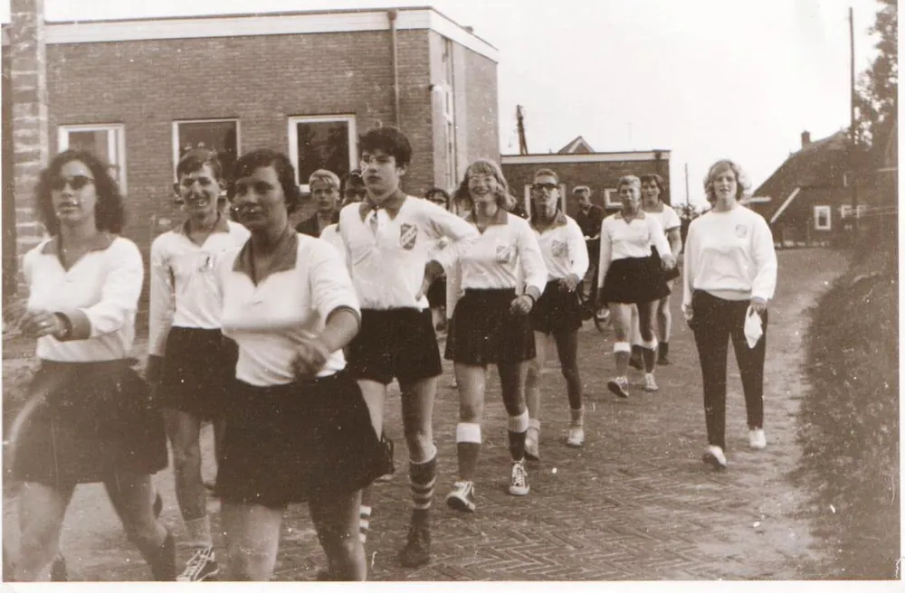 Een groep spelers en speelsters in clubtenue loopt door een straat