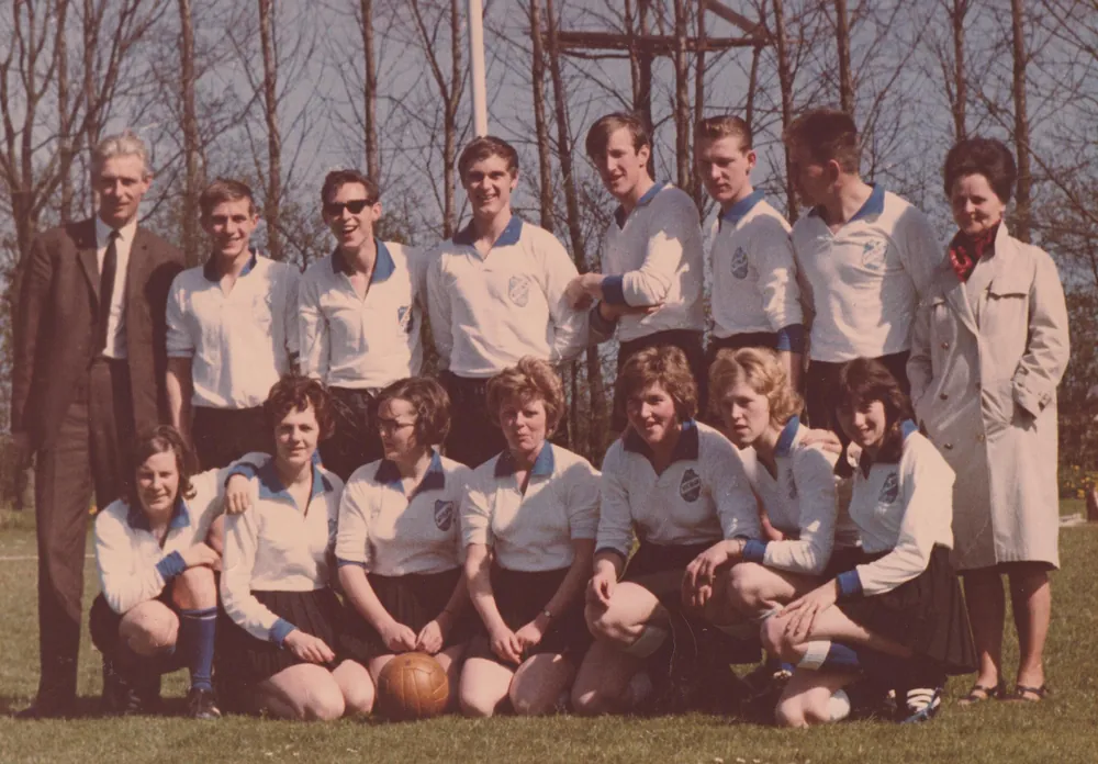 Teamfoto van spelers in witte shirts met een bal, met begeleiders erbij