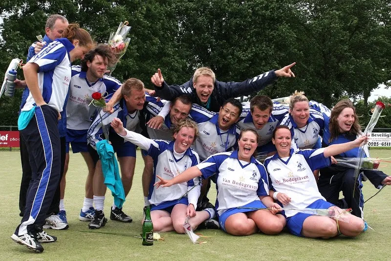 Spelers en speelsters vieren een kampioenschap op het veld, met bloemen en champagne