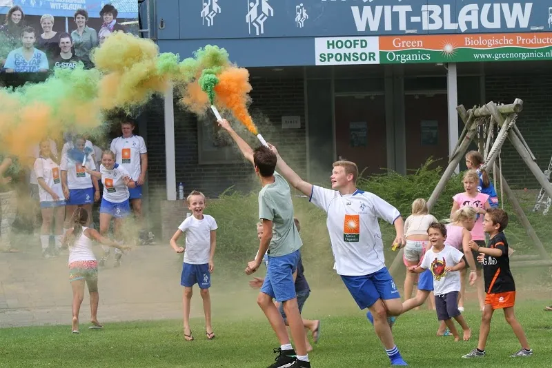 Kinderen rennen over het veld met wit-blauwe en oranje kleurrook