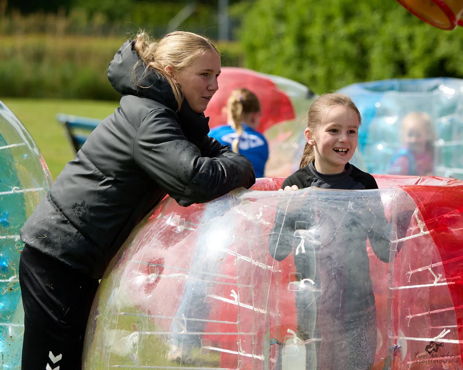 Een trainster en een lachend meisje bij de bubbelballen tijdens een clubactiviteit