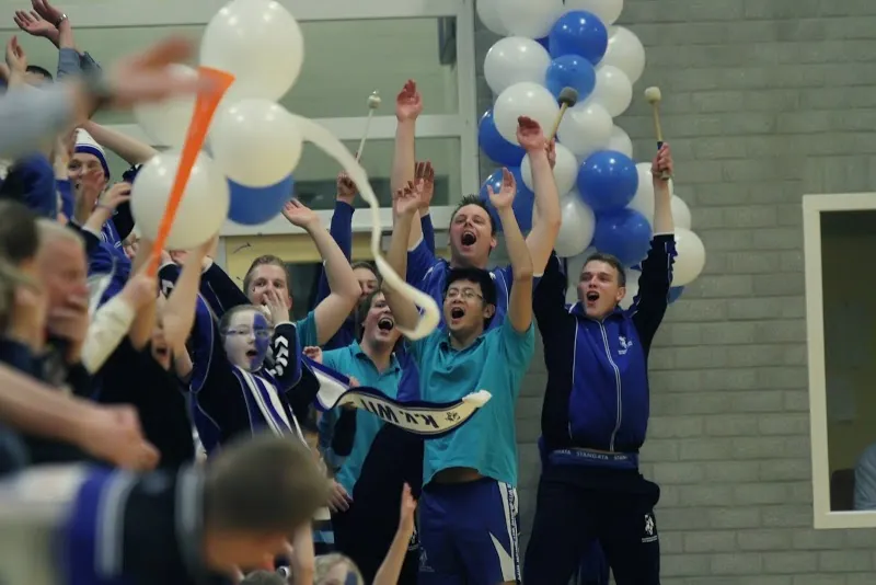 Juichende supporters met wit-blauwe ballonnen en toeters