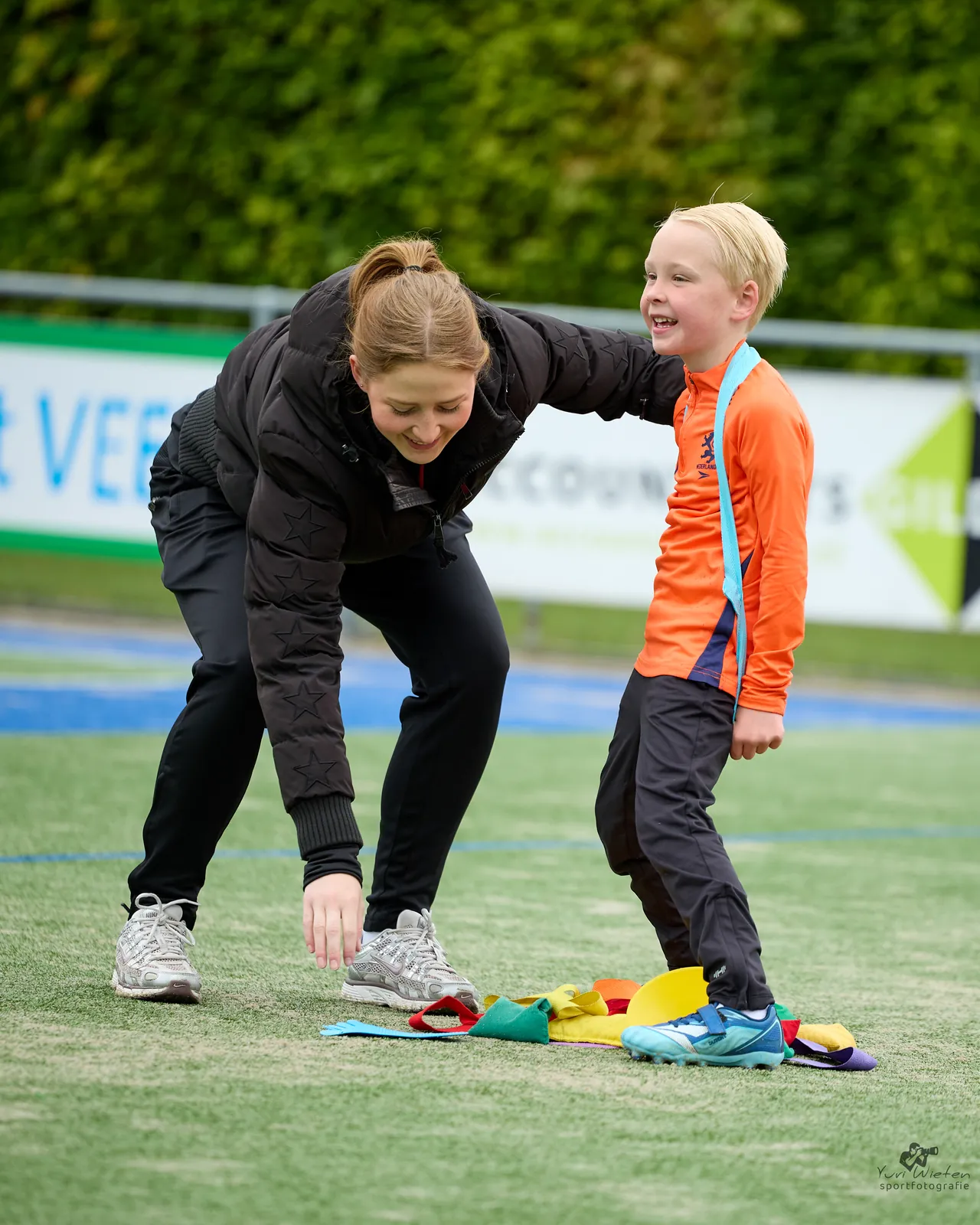 Een trainster doet een oefening voor aan een jonge speler op het veld